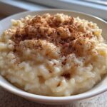 Close-up of a white bowl filled with creamy rice pudding, topped generously with ground cinnamon.