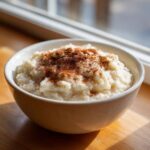 A close-up of a bowl of creamy rice pudding recipe dusted generously with cinnamon.