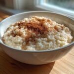 A white bowl filled with creamy rice pudding recipe, generously sprinkled with ground cinnamon.