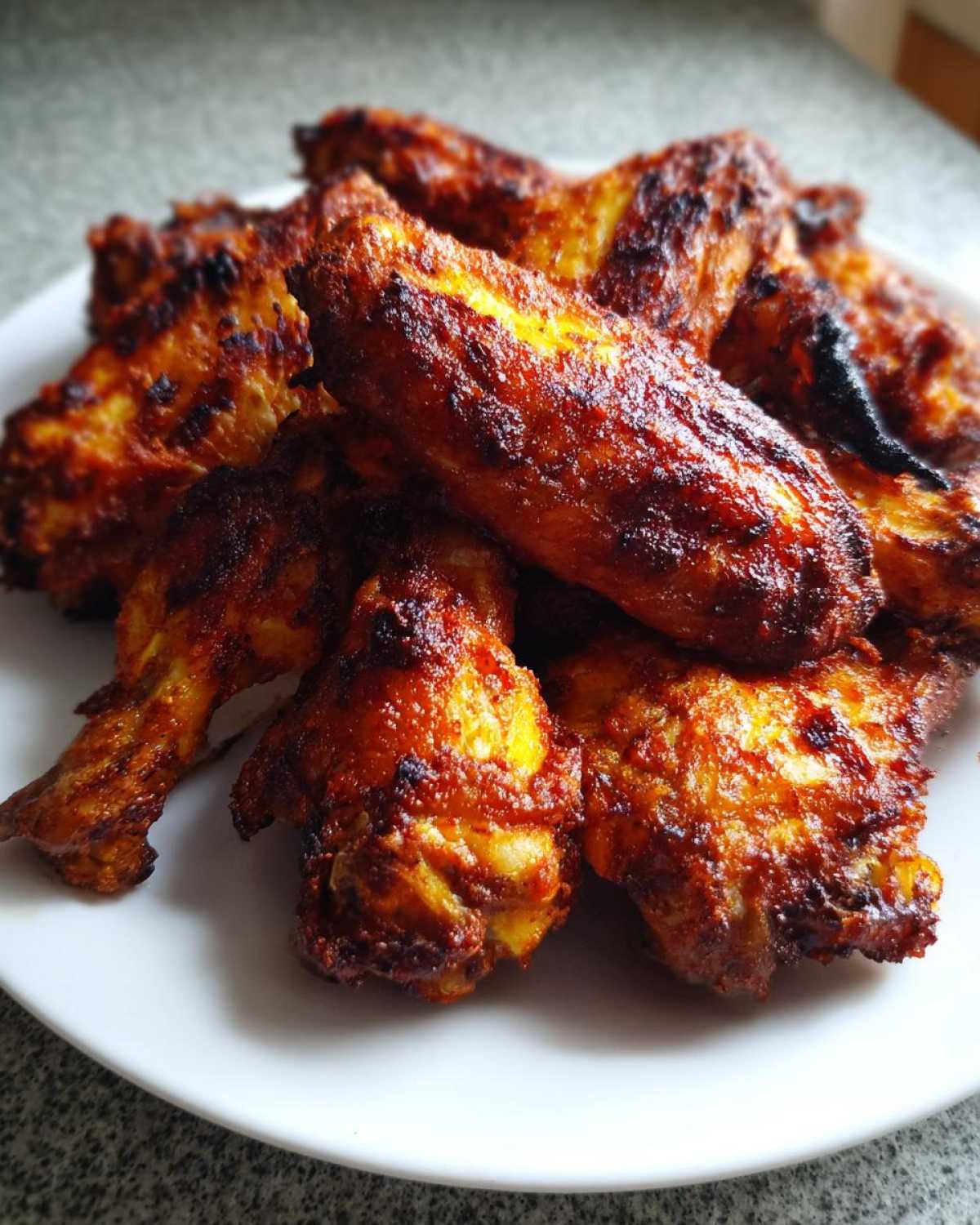 A close-up of a pile of deeply browned, crispy baked chicken wings served on a white plate.