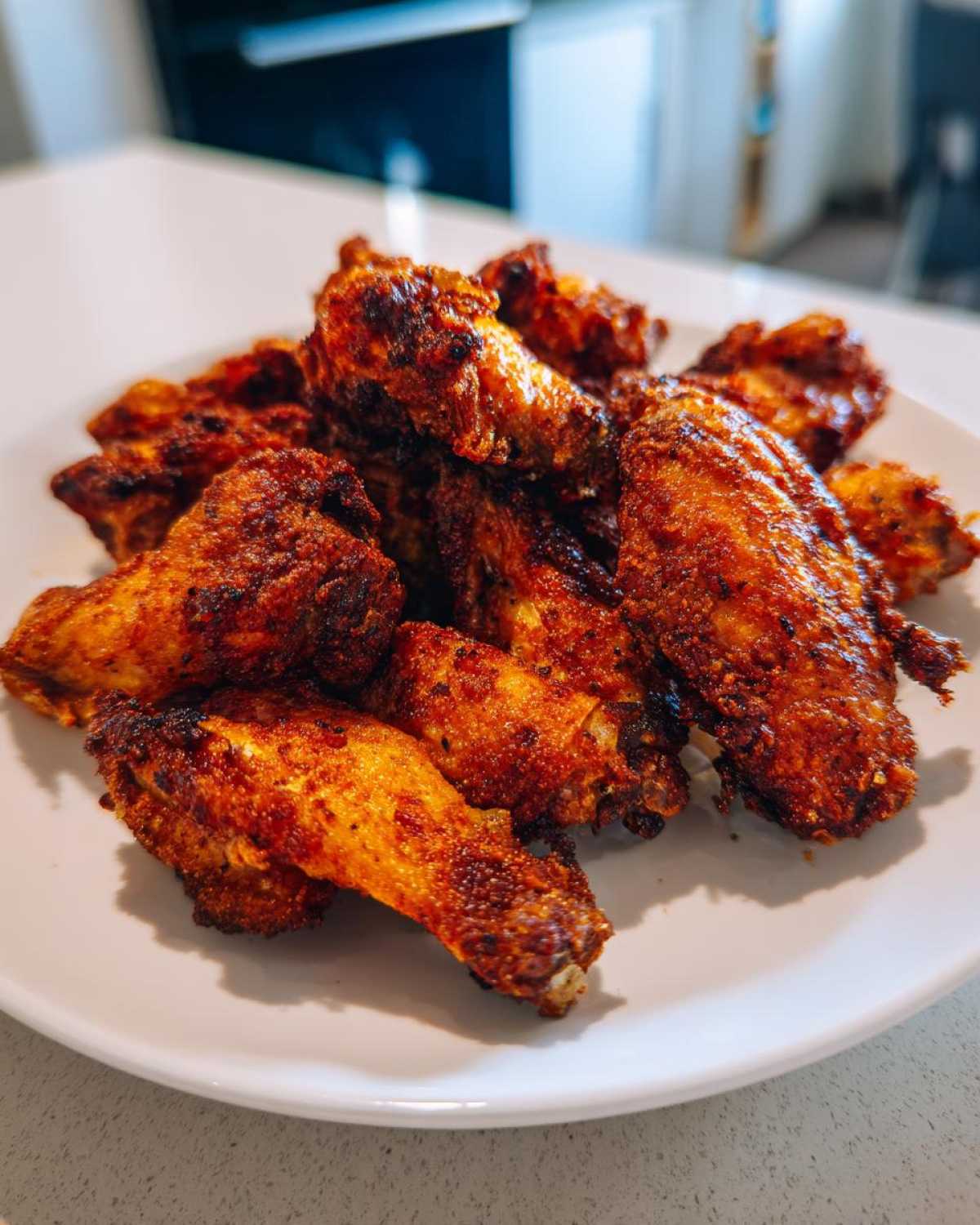 A mound of perfectly seasoned and crispy baked chicken wings piled high on a white plate.