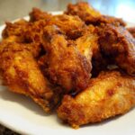A close-up of a white plate piled high with golden brown, crispy baked chicken wings.