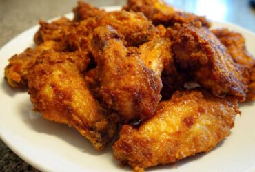 A close-up of a white plate piled high with golden brown, crispy baked chicken wings.