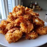 A large pile of golden brown, crispy fried shrimp served on a white plate.