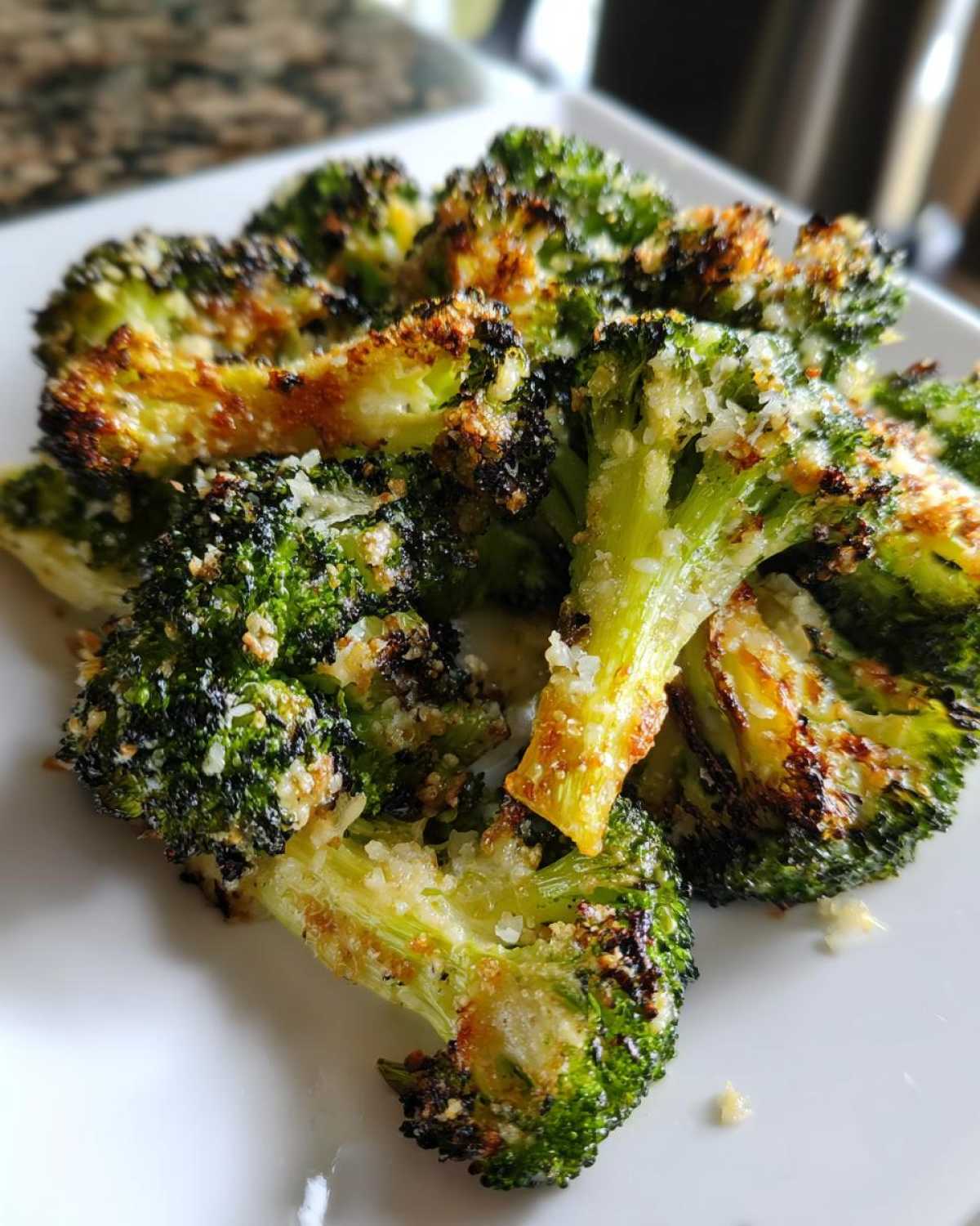 Close-up of perfectly roasted broccoli florets topped with browned Parmesan cheese.