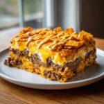 A thick, layered slice of Dorito Casserole topped with melted cheese and a sour cream drizzle.