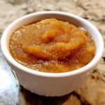 A close-up shot of rich, spiced homemade applesauce served in a small white ramekin.