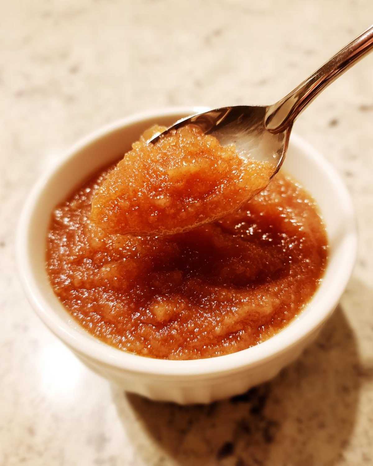 A spoonful of chunky, homemade applesauce being lifted from a small white bowl.