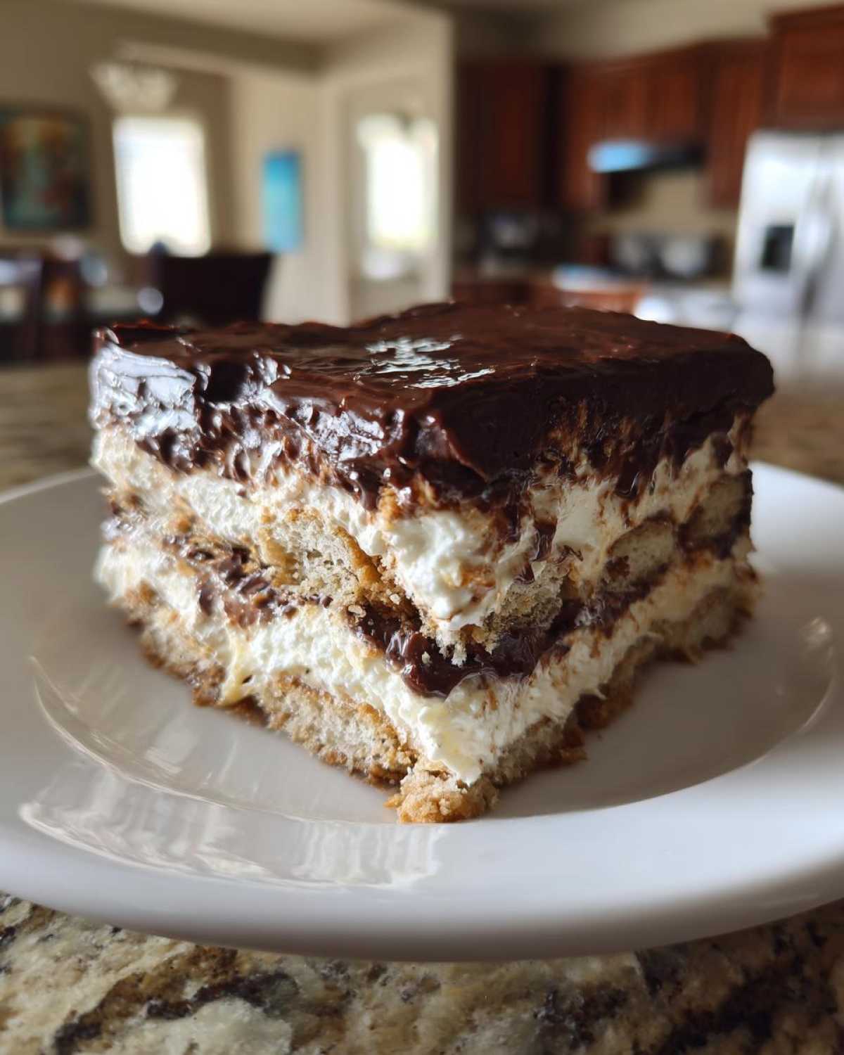 A close-up of a layered slice of eclair cake with graham crackers, creamy filling, and chocolate frosting.