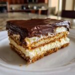 Close-up of a layered slice of eclair cake featuring graham crackers, vanilla cream filling, and chocolate frosting.