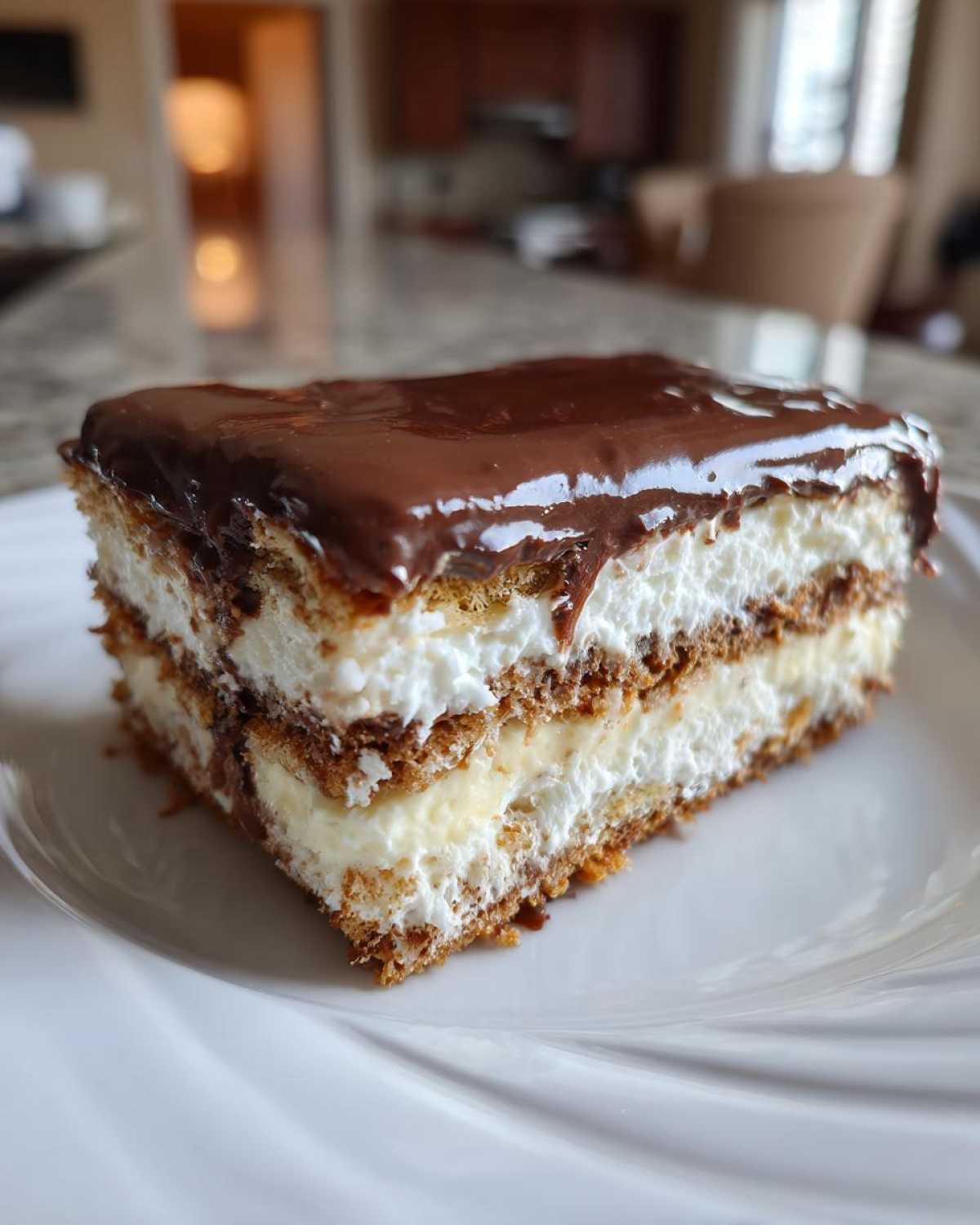 A perfect square slice of eclair cake showing layers of graham crackers, cream filling, and rich chocolate glaze.