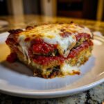 A close-up of a thick, cheesy slice of eggplant parmesan layered with marinara sauce on a white plate.