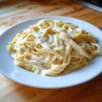 A serving of fettuccine pasta generously coated in creamy homemade alfredo sauce and sprinkled with black pepper.