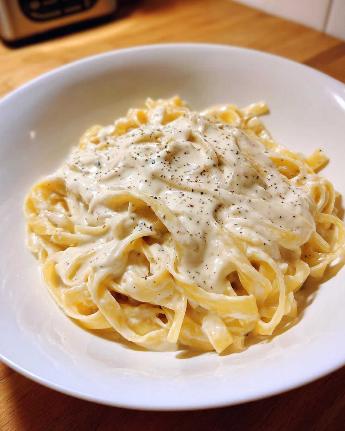 Close-up of fettuccine pasta generously coated in rich homemade alfredo sauce and topped with cracked black pepper.