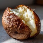 Close-up of a perfectly cooked air fryer baked potato split open to show fluffy white interior and crispy brown skin.