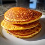 A close-up of a tall stack of three golden-brown, fluffy almond flour pancakes on a white plate.