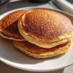 A stack of three golden-brown, fluffy almond flour pancakes on a white plate.