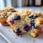 Close-up of a fluffy blueberry muffin cut in half, showing moist crumb and streusel topping.