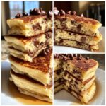 A tall stack of fluffy chocolate chip pancakes, cut to show melted chips inside, topped with more chocolate chips.