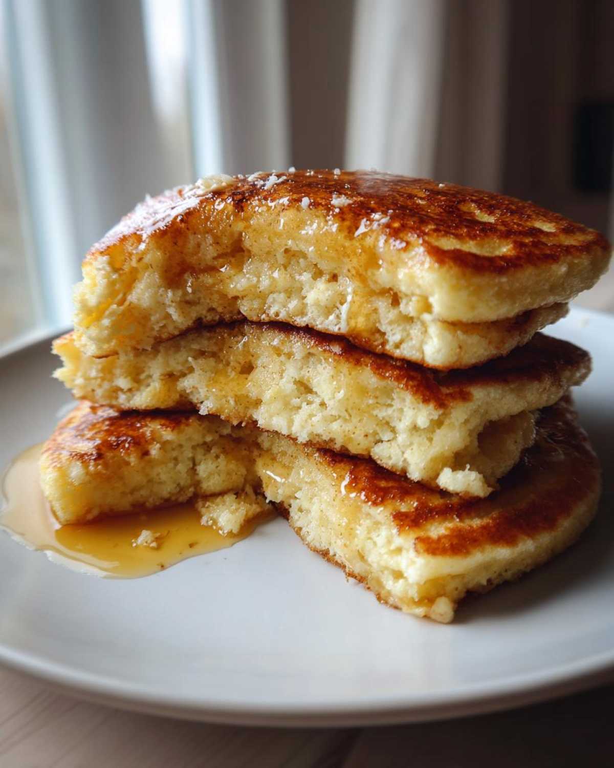 Close-up of a stack of fluffy coconut flour pancakes cut open, drizzled generously with syrup.