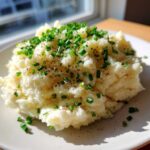A mound of creamy garlic mashed potatoes topped generously with fresh chopped chives and black pepper.