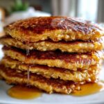 A tall stack of four fluffy oatmeal pancakes covered in glistening syrup dripping down the sides.