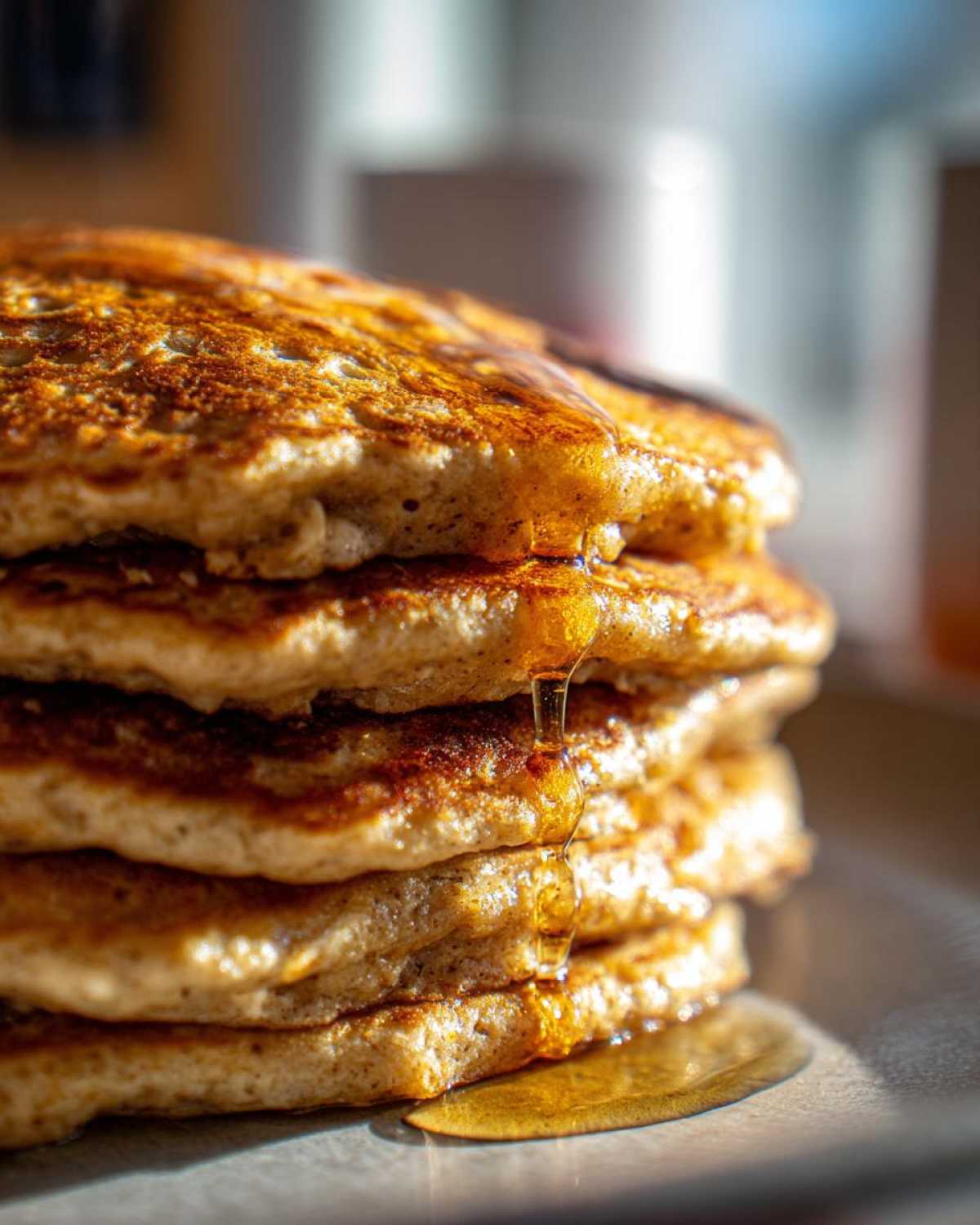 Close-up of a tall stack of fluffy oatmeal pancakes with syrup dripping down the side.