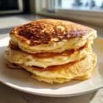 A tall stack of three golden brown, incredibly fluffy pancakes drizzled with syrup, sitting on a white plate.