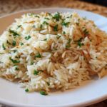 A close-up of fluffy rice pilaf, mixed with toasted vermicelli and garnished with fresh parsley, served on a white plate.