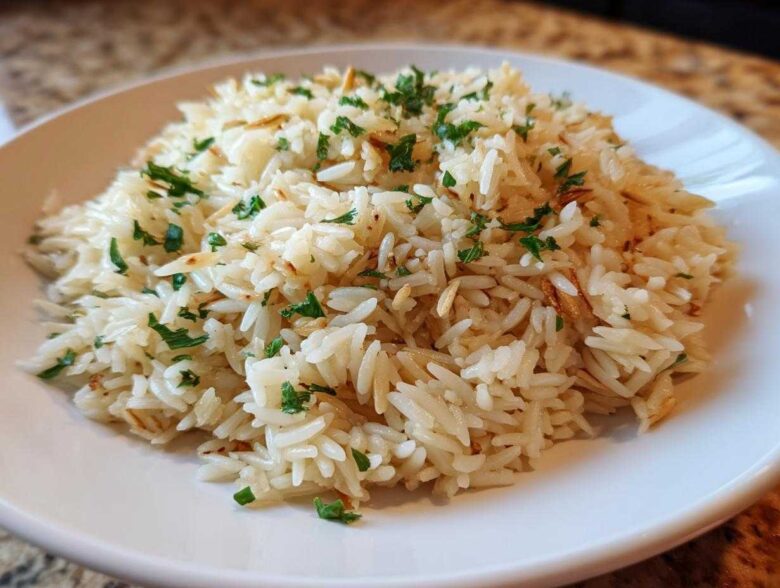 A close-up of fluffy rice pilaf, mixed with toasted vermicelli and garnished with fresh parsley, served on a white plate.