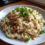 A close-up of fluffy rice pilaf served on a white plate, garnished with fresh parsley and crispy fried onions.