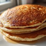 A close-up stack of three fluffy sourdough discard pancakes glistening with syrup.