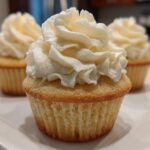Close-up of a perfectly baked vanilla cupcake topped with a swirl of creamy white vanilla frosting.