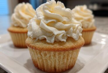 Close-up of a perfectly baked vanilla cupcake topped with a swirl of creamy white vanilla frosting.