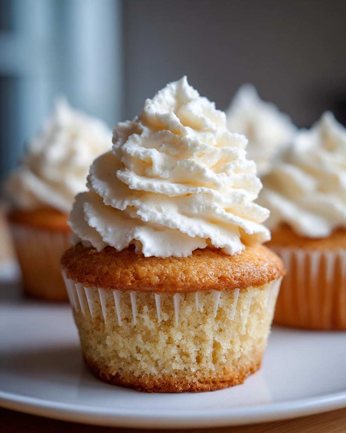Close-up of a perfectly baked vanilla cupcake topped with a tall swirl of white frosting.