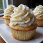 Close-up of a fluffy vanilla cupcake topped with perfectly swirled white vanilla frosting.