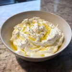 A close-up of creamy, fluffy whipped feta dip topped with golden olive oil and herbs.