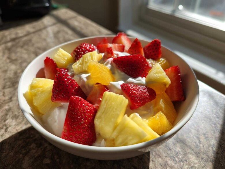 A white bowl filled with fresh strawberries, pineapple chunks, and orange segments served over a creamy fruit dip.