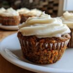 A close-up of a moist carrot cake muffin topped with thick cream cheese frosting, part of a batch of amazing carrot cake muffins.