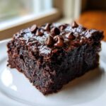 Close-up of a fudgy square of black bean brownies topped with melted chocolate chips on a white plate.