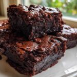 Close-up of fudgy black bean brownies stacked on a white plate, topped with melted chocolate chips.