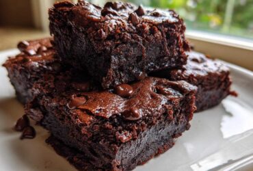 Close-up of fudgy black bean brownies stacked on a white plate, topped with melted chocolate chips.