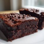 Two fudgy sweet potato brownies topped with chocolate chips served on a white plate.