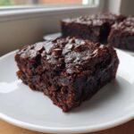 Close-up of a fudgy slice of sweet potato brownies topped with melted chocolate chips on a white plate.