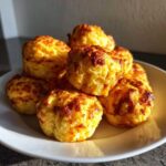 A stack of freshly baked, golden brown egg bites with crispy tops served on a white plate.