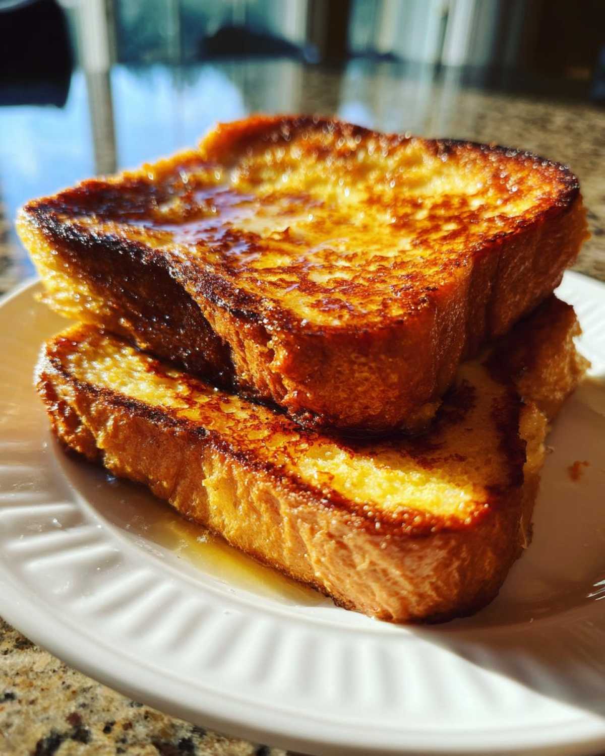 Close-up of two thick slices of golden brown french toast stacked on a white plate, drizzled with syrup.