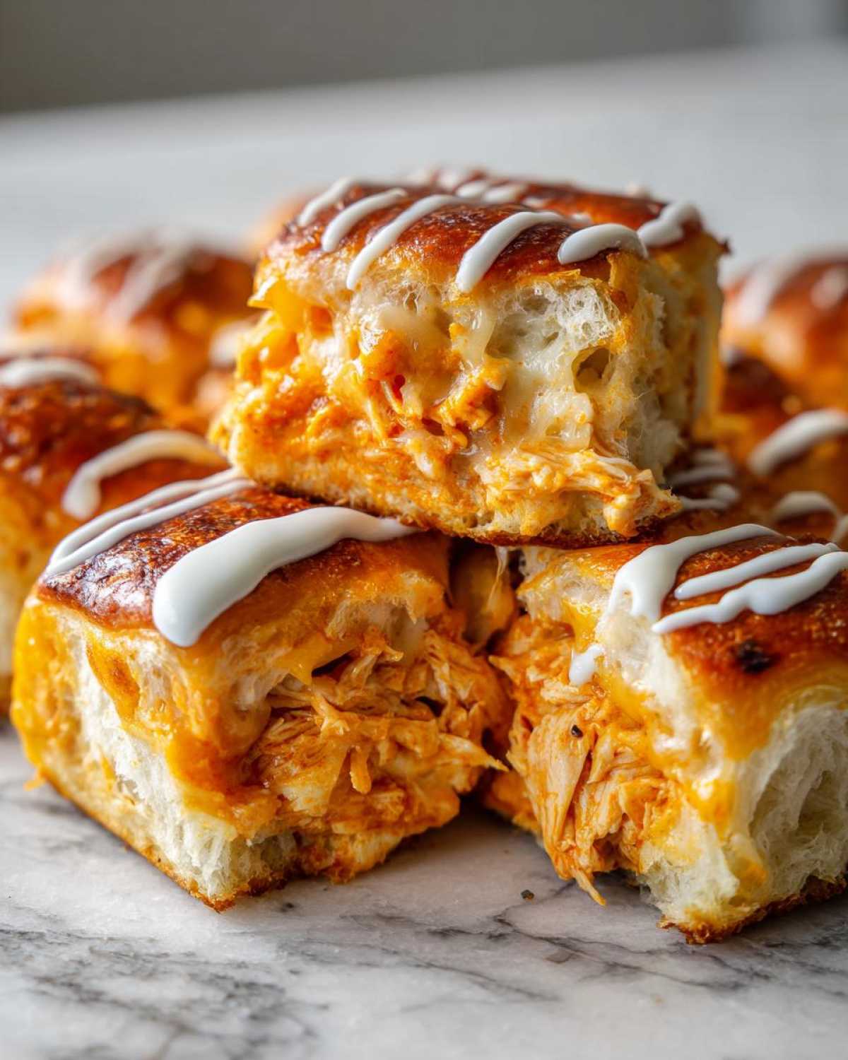 Close-up of gooey buffalo chicken sliders stacked, showing shredded chicken filling and white icing drizzle.