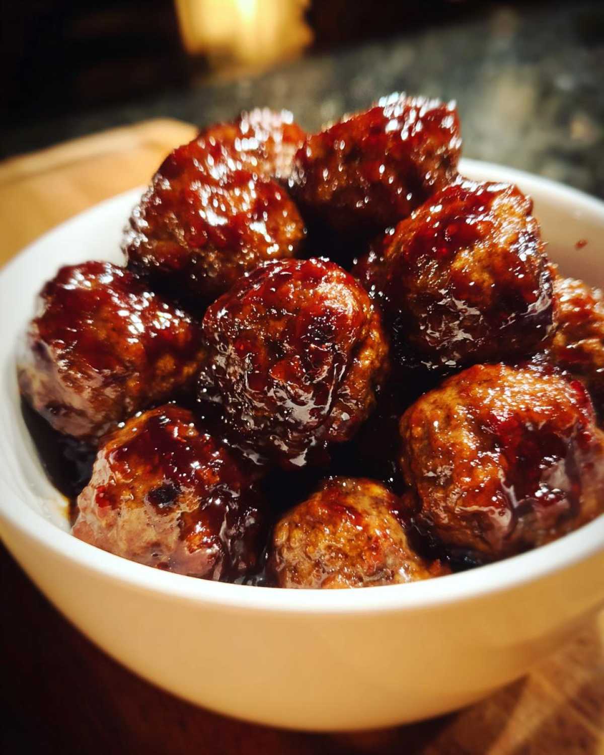 A close-up of glossy, saucy grape jelly meatballs served in a small white bowl.
