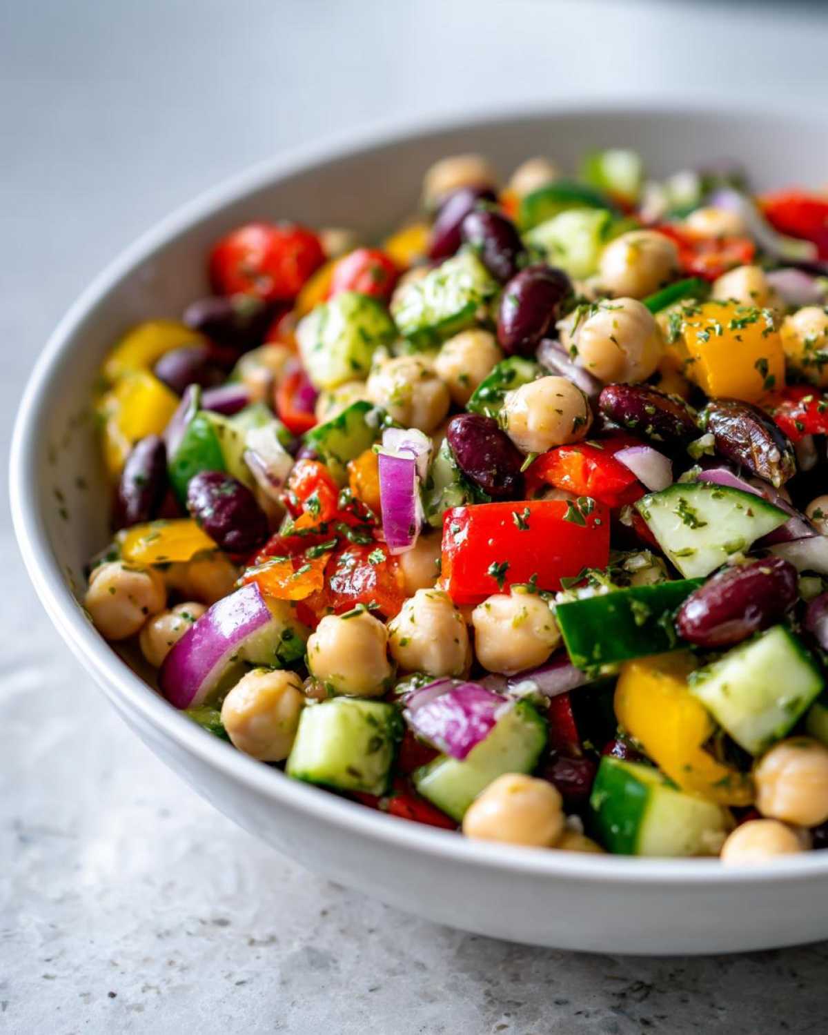 Close-up of a colorful, high-protein bean salad featuring chickpeas, kidney beans, cucumber, red onion, and bell peppers.