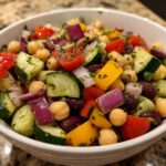 A vibrant, close-up view of a high protein bean salad featuring chickpeas, kidney beans, cucumbers, red onion, and bell peppers in a white bowl.